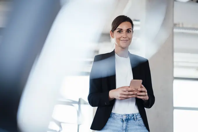 Confident businesswoman holding smart phone at office