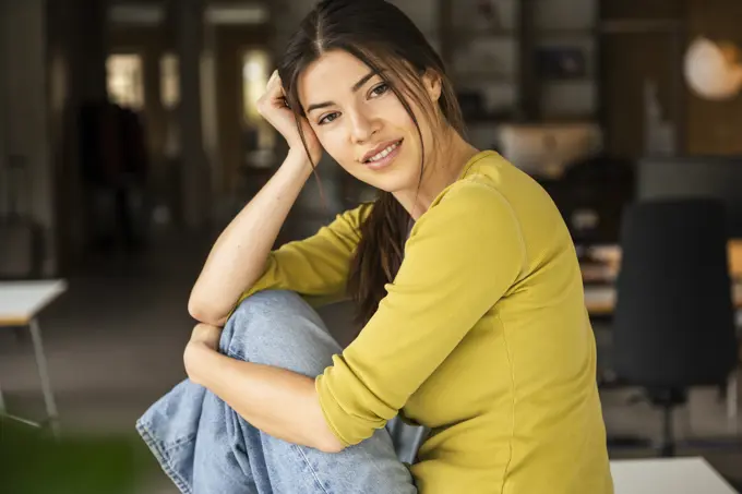 Young businesswoman with head in hand sitting on desk at work place