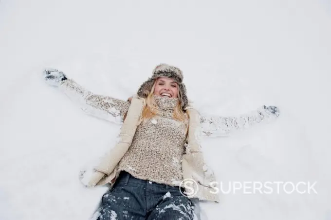 Austria, Salzburg County, Mid adult woman lying on snow, smiling