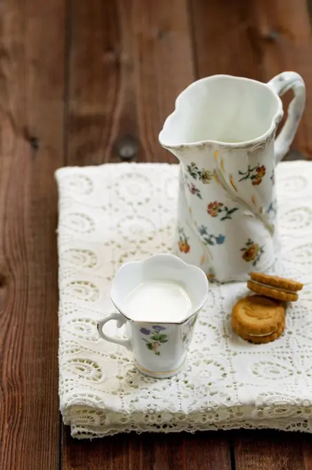 Cup of milk, milk pitcher and cookies on white tablecloth