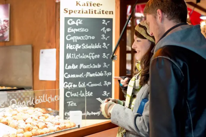 Germany, Berlin, young couple buying deep-fried pastries at Christmas market