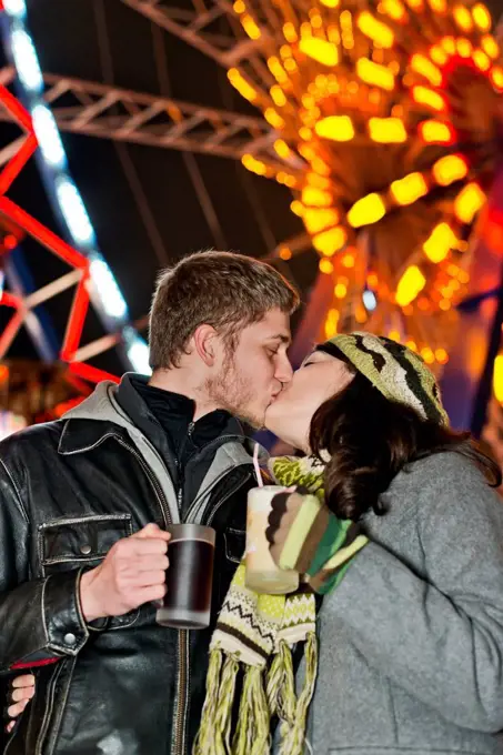 Germany, Berlin, happy young couple kissing at Christmas market in front of lighted big wheel