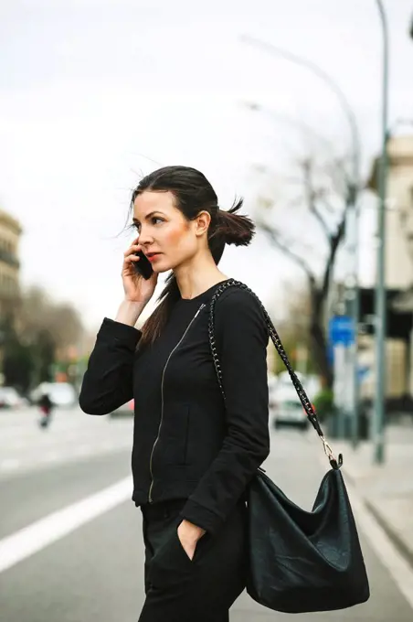 Spain, Catalunya, Barcelona, young black dressed businesswoman telephoning in front of a street