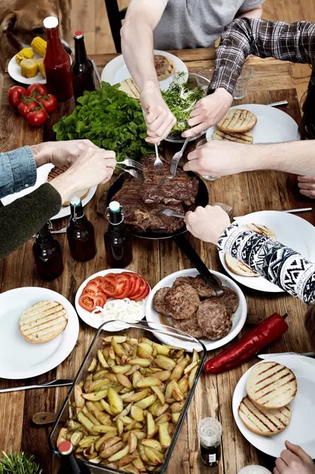 Friends eating potatoes, steaks and meatballs at wooden table