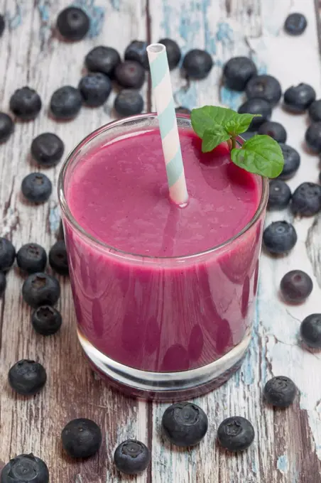 Glass of blueberry smoothie and blueberries on wood
