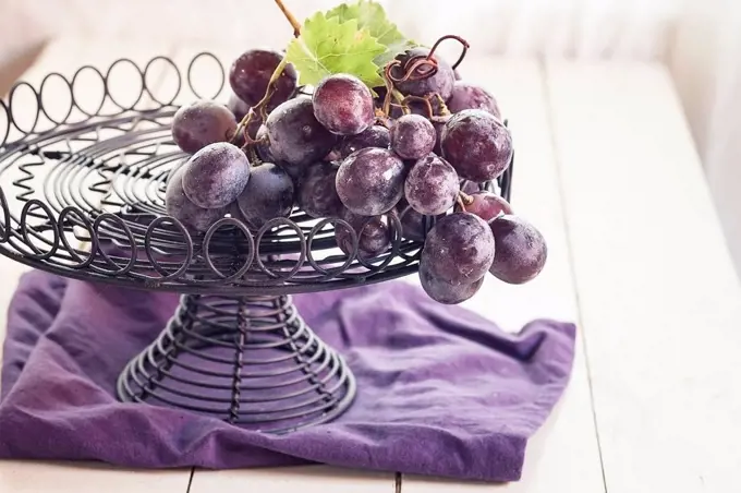 Wire fruit bowl of blue grapes on purple cloth