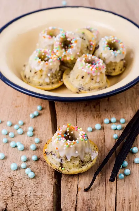 Bowl of mini vanilla marble cakes, pearls and vanilla pods on wood