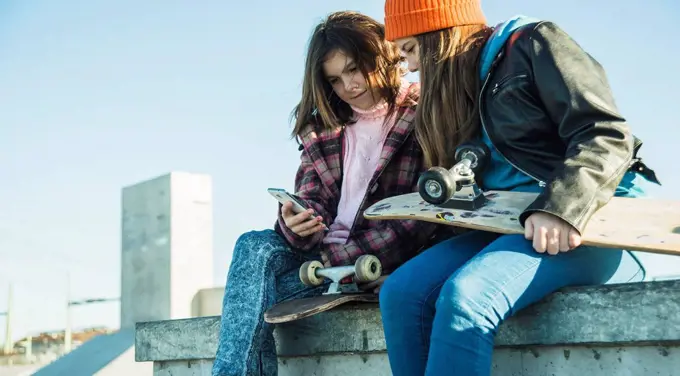 Two girls in skatepark sharing cell phone