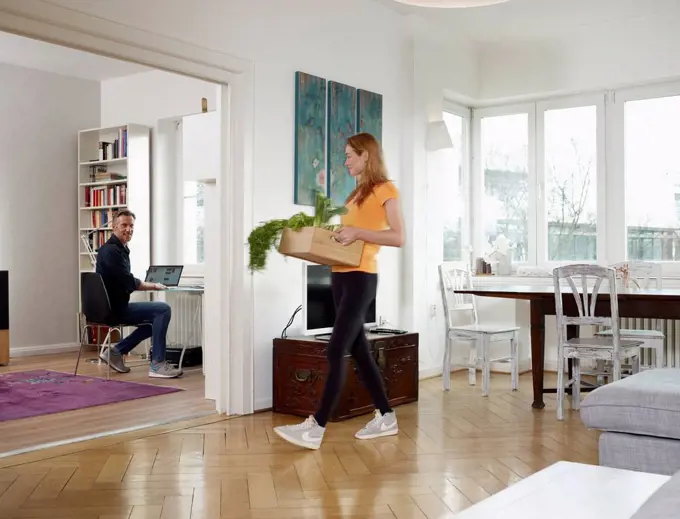 Mature man working from home, adult daughter carrying box with vegetables