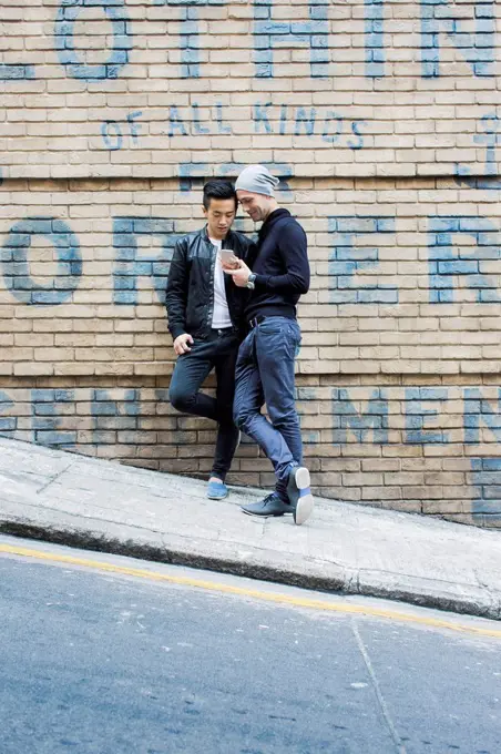 China, Hong Kong, gay couple at house wall looking on cell phone