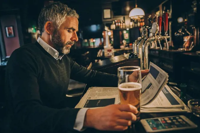 Man sitting at counter of a pub reading newspaper