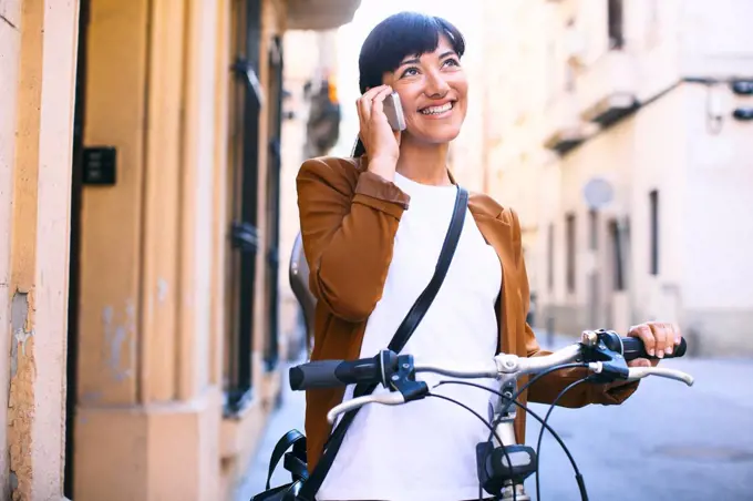 Spain, Barcelona, smiling woman with bicycle and cell phone in the city