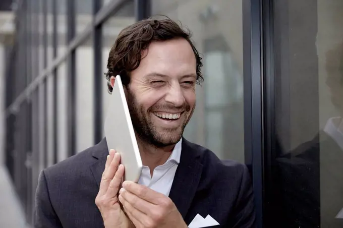 Portrait of laughing businessman trying to phone with his digital tablet