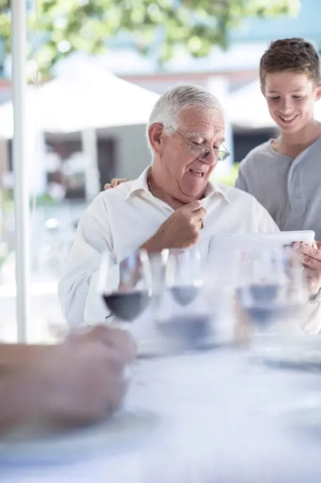 Grandfather and grandson using digital laptop at restaurant