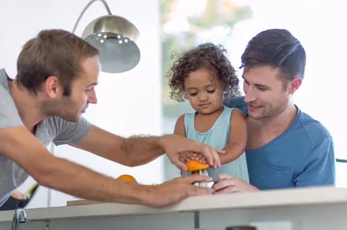 Gay couple with daughter making orange juice