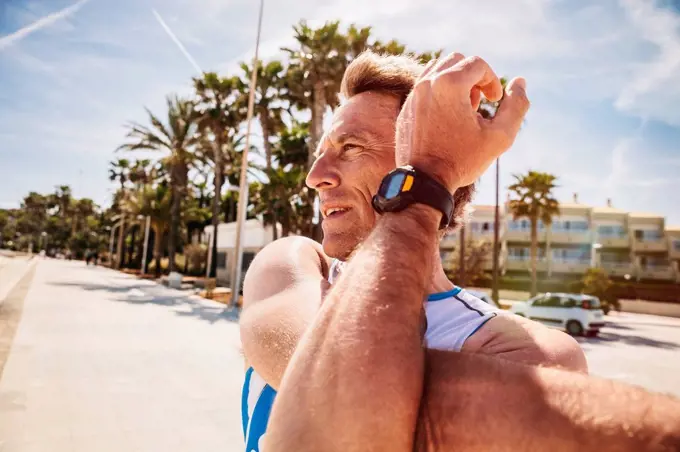 Spain, Mallorca, Sa Coma, triathlet stretching on the beach promenade