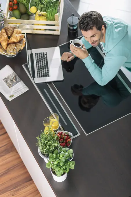 Man with cup of coffee and laptop in the kitchen