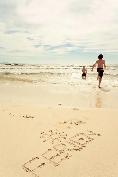 Spain, Mallorca, Two young boys at the beach running into the seawater, word Ferien written in the sand