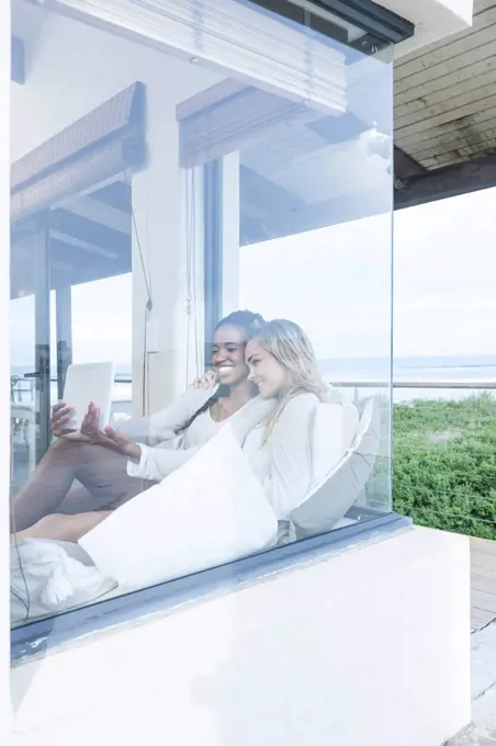 Two young women with digital tablet relaxing in beach house