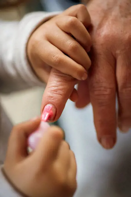 Little girl painting her grandmother's finger nails