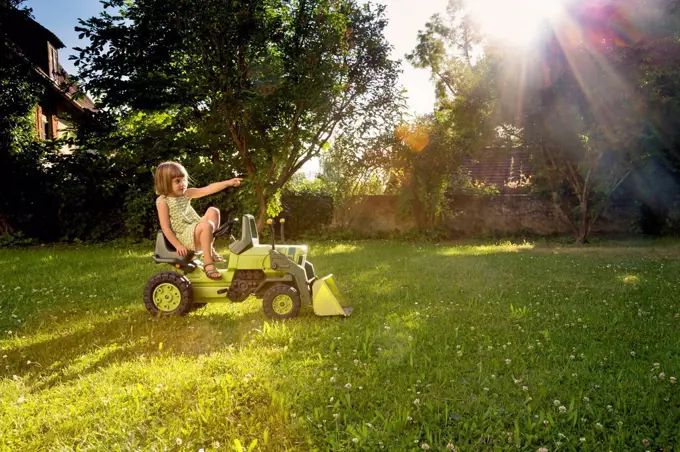 Little girl playing with toy tractor in a garden