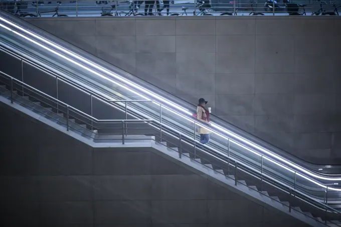 Young woman with coffee to go standing on escalator