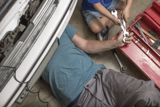 Son helping father in home garage working on car