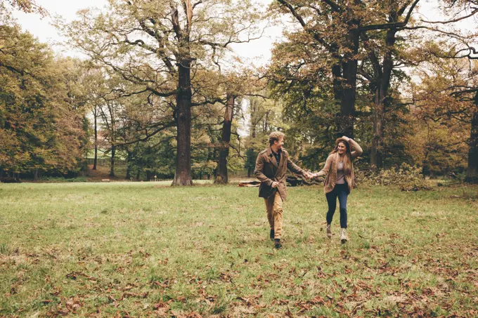 Young couple in love holding hands and running in an autumnal park