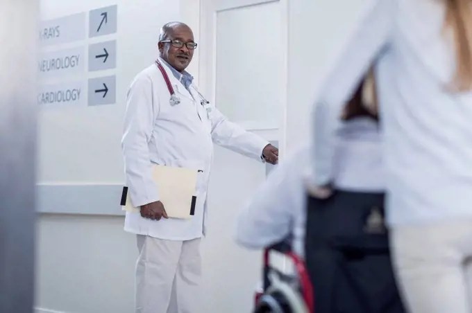 Doctor in hospital corridor opening door and patient in wheelchair