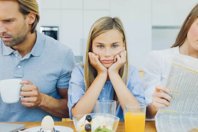 Frustrated girl with distracted parents at breakfast table