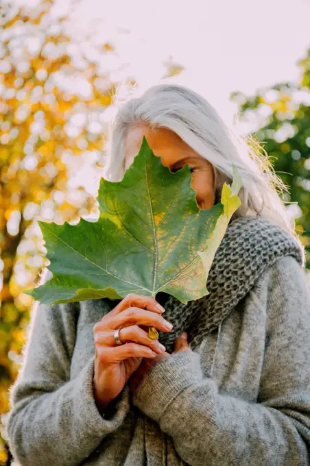 Woman hiding her face behind an autumn leaf