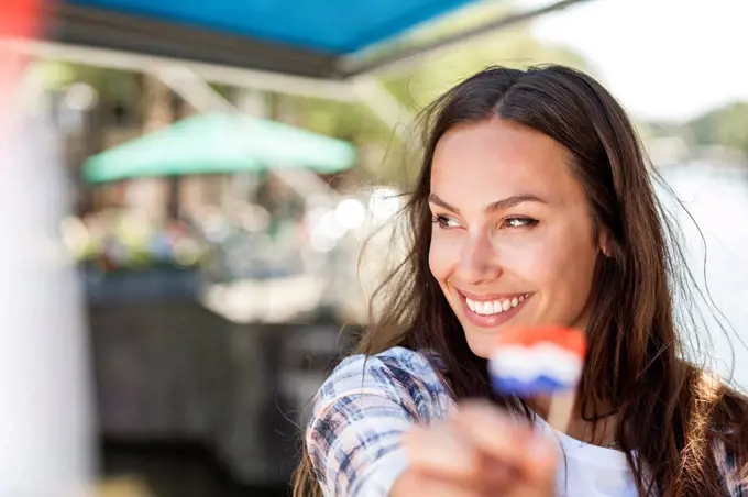 Netherlands, Amsterdam, smiling young woman holding small Dutch flag