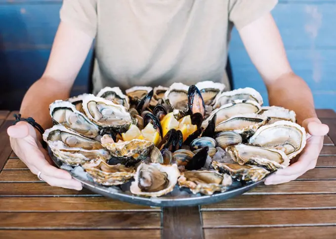 Man's hands holding a seafood platter with oysters, clams and mussels.