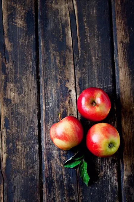 Three red apples and leaves on dark wood