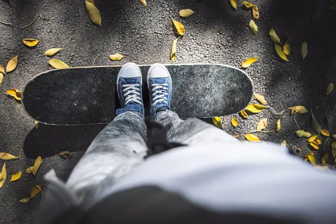 Boy standing on skateboard on path with autumn leaves