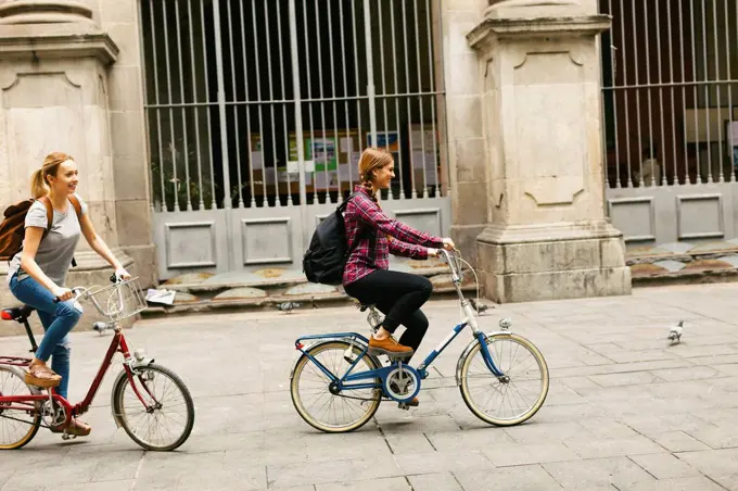 Spain, Barcelona, two young women riding bicycle in the city