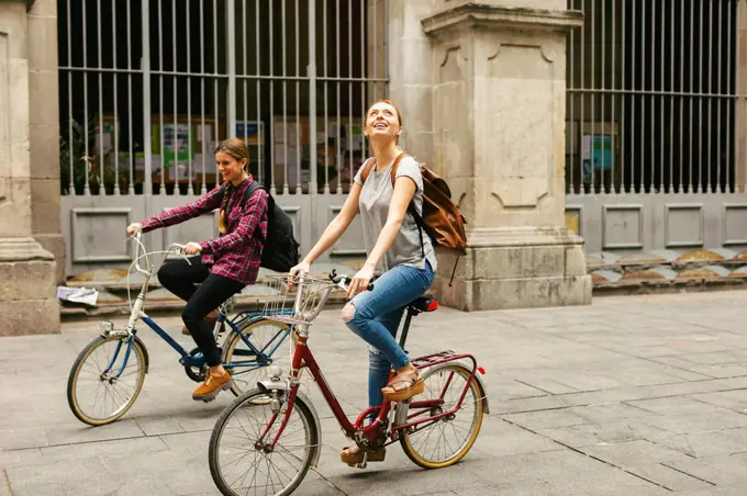 Spain, Barcelona, two young women riding bicycle in the city