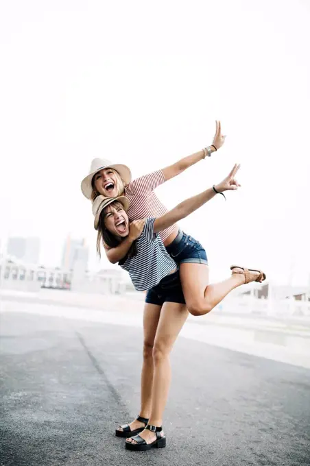 Spain, Barcelona, young woman giving her friend a piggyback ride