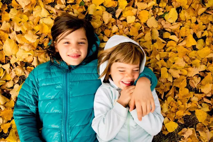 Two girls lying side by side on ground covered with autumn leaves