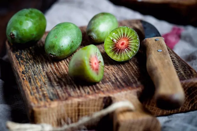 Sliced and whole mini kiwis and kitchen knife on wooden chopping board