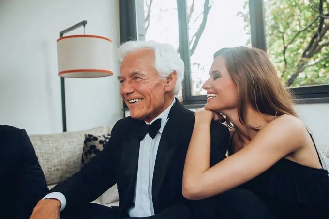 Smiling young woman with elegant senior man on couch