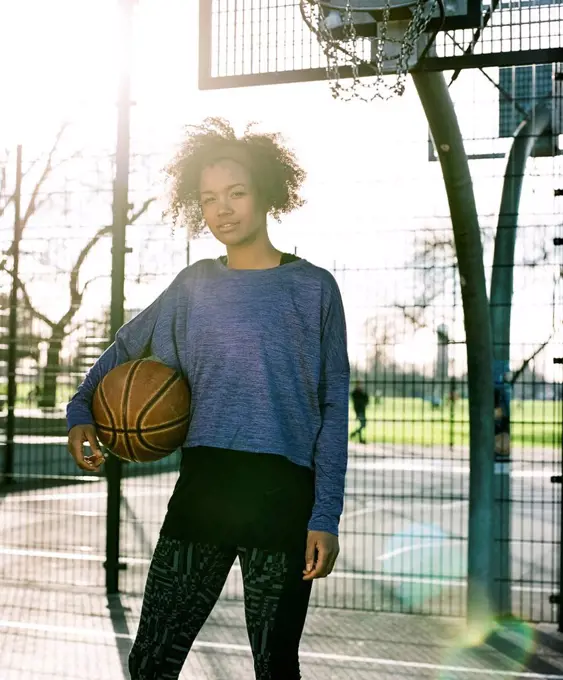 Portrait of young woman with basketball at backlight