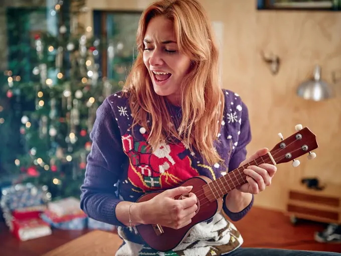 Blond woman playing ukulele in front of Christmas tree