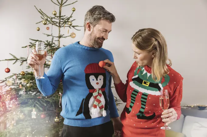 Two people with ugly Christmas sweaters laughing in front of tree