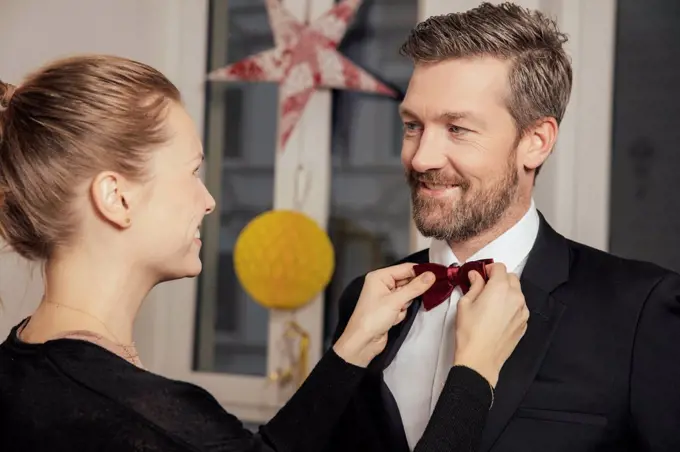 Couple preparing for New Year's Eve party, fastening bow tie