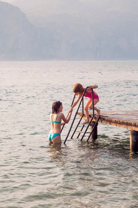 Italy, Brenzone, girl helping her little sister from jetty into the lake