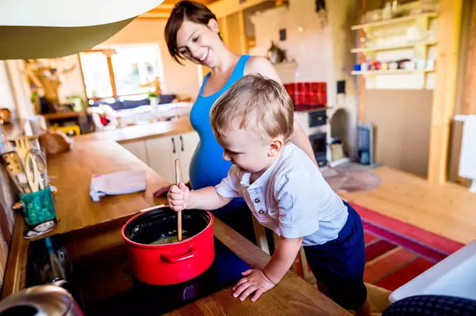 Little boy helping his pregnant mother to cook, stirring in pot