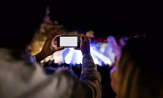 Back view of young man taking pictures with smartphone at summer concert