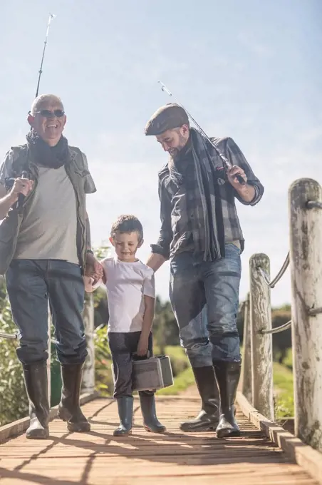 Grandfather, father and son walking over bridge with fishing equipment