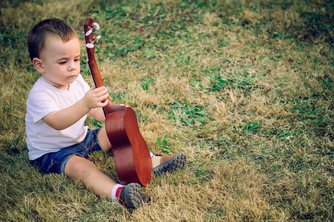 Baby boy sitting on a meadow with ukulele